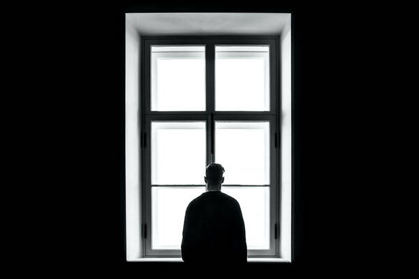 Image of black-and-white, backlit person looking out a window
