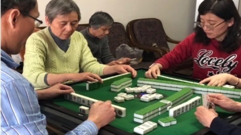 photo of four adults seated at a table, examining sets of tiles, engaged in playing the game of mahjong