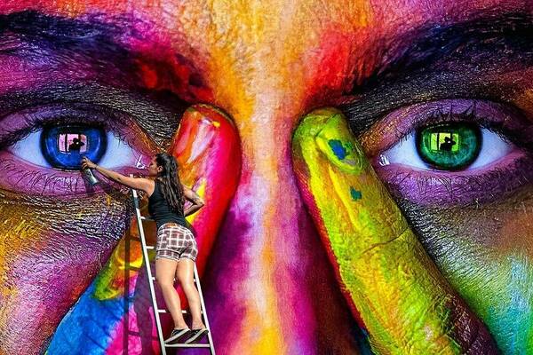 multi-colored closeup of human face mural with painter at work