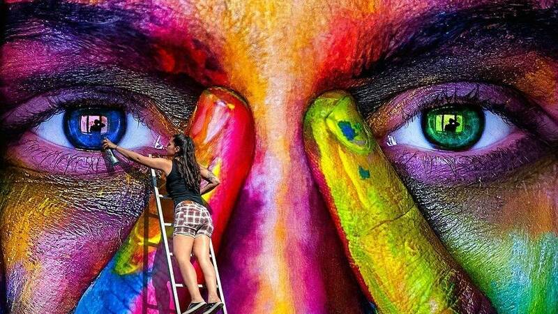 multi-colored closeup of human face mural with painter at work