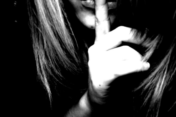 grainy black and white photo of woman's mouth and chin, with finger to her lips, mouthing "shh!"