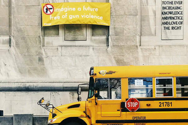 Image of a sign calling for an end to gun violence, and a school bus driving by below it