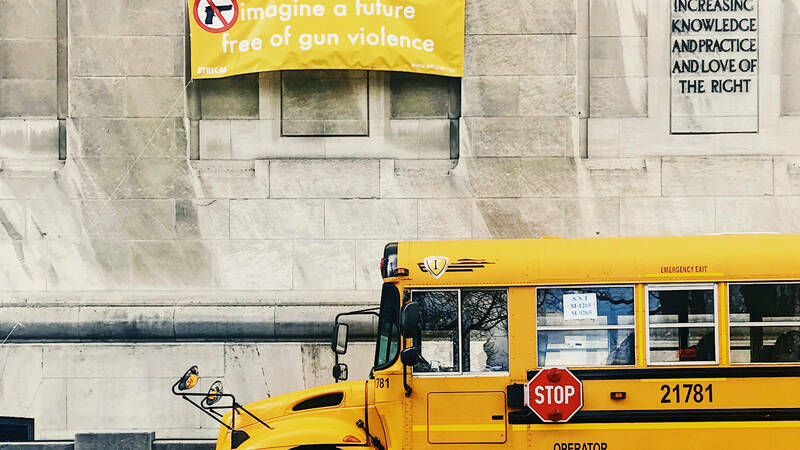 Image of a sign calling for an end to gun violence, and a school bus driving by below it