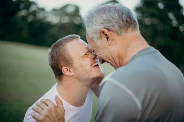 A boy with down syndrome smiling up at his father with their foreheads pressed together