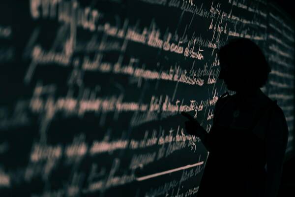 Image of figure in silouette at a blackboard doing work