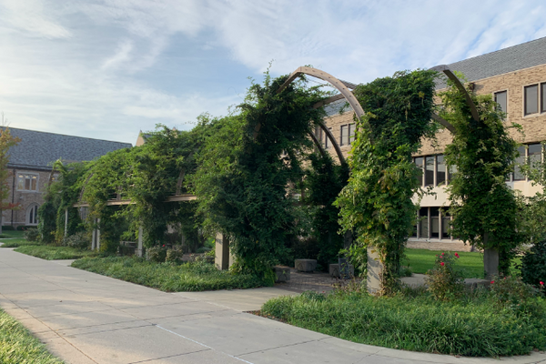 Photo of an arched structure with greenery in front of a brick building on the Notre Dame campus