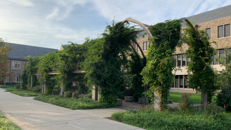 Photo of an arched structure with greenery in front of a brick building on the Notre Dame campus