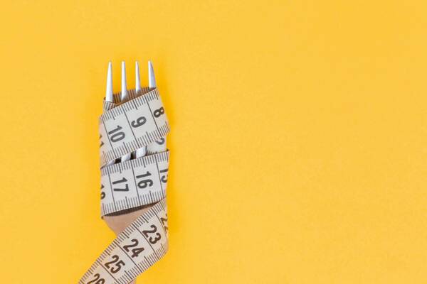 Fork wrapped with a tape measure against a bright yellow background.