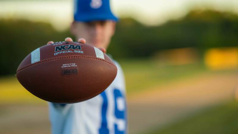 A focused image of a football labeled NCAA held by a blurry man