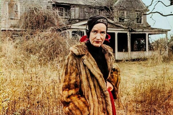 a woman in a fur coat standing in front of a dilapidated house