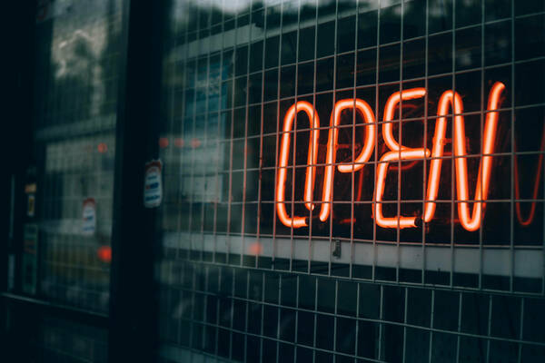 Neon sign saying "open" in a window with a protective grate