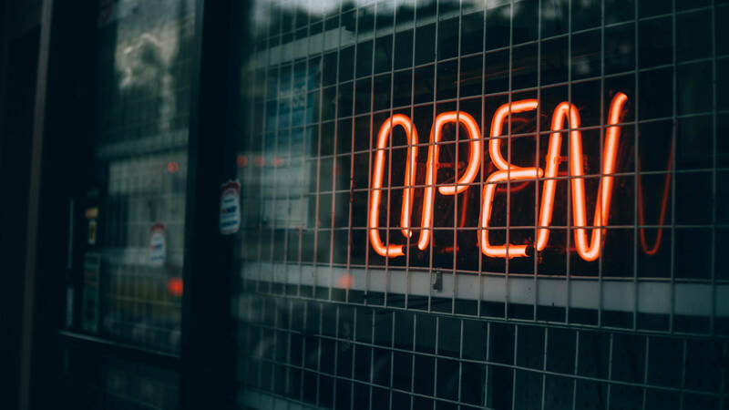 Neon sign saying &quot;open&quot; in a window with a protective grate