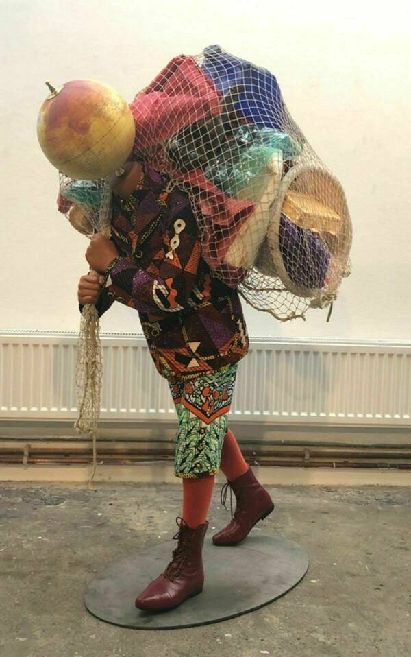 A sculpture of a child carrying a mesh bag full of items