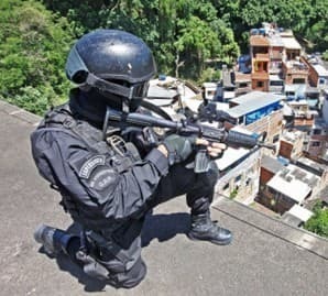 a police officer crouching on a roof aiming his long gun downwards