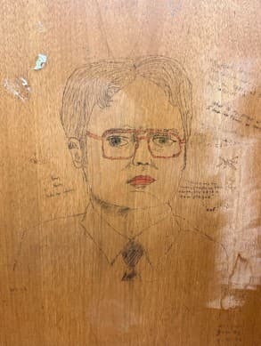 a drawing of Dwight Schrute on a desk with writing around him