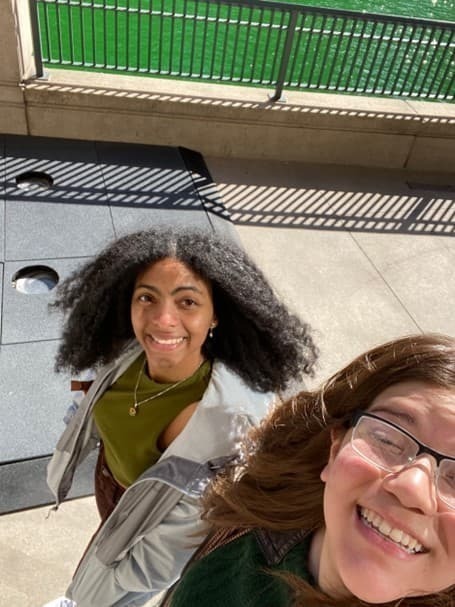 a selfie of two smiling young women one with black curly hair, the other with brown hair and glasses