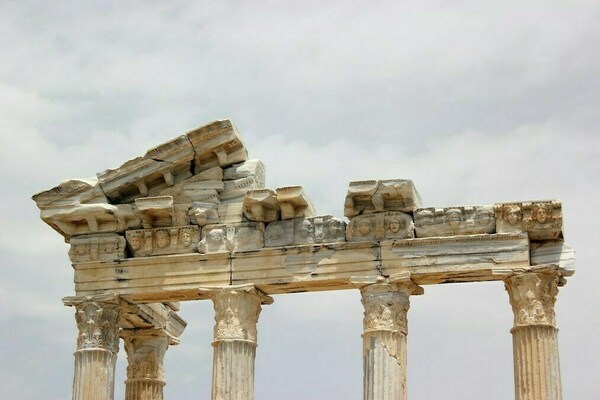 Pillars from a historical building that is crumbling set against a cloudy sky