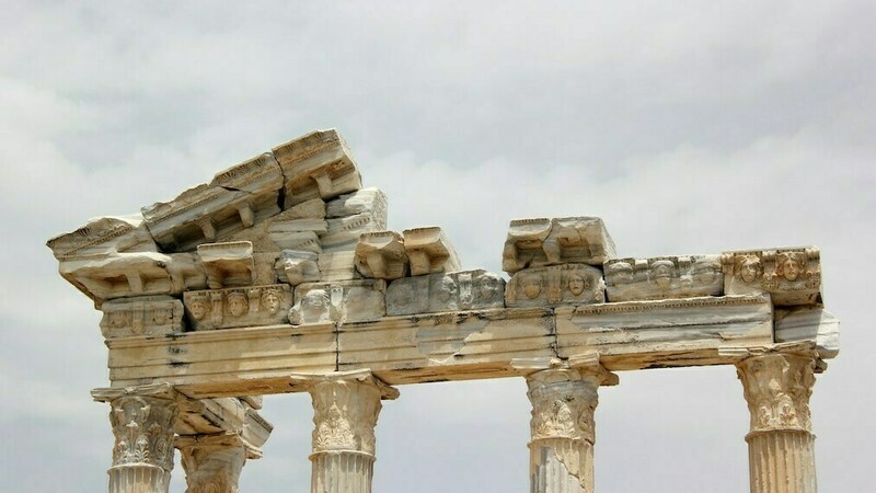 Pillars from a historical building that is crumbling set against a cloudy sky