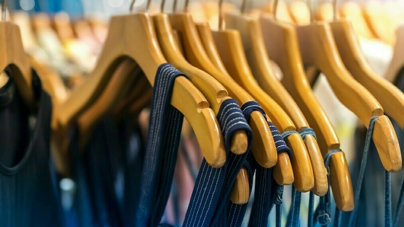 Close up of wooden clothes hangers on a rack holding blue colored clothing