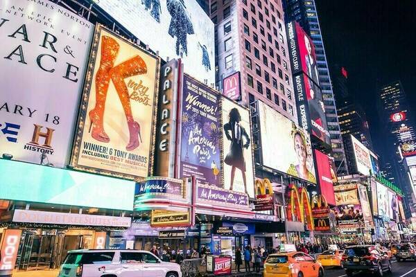 New York theater district with flashing lights, taxis, and lit up billboards for plays and musicals