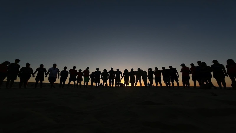 a line of people in silhouette watching a sunrise
